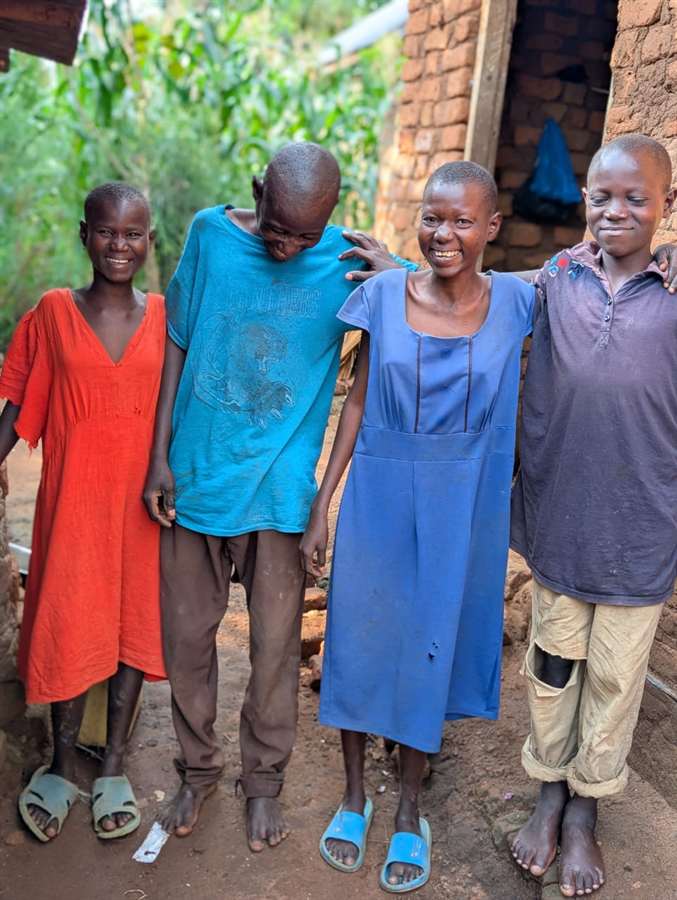 Young people from the Ugandan community standing together outside their homes, representing the families the medical clinic campaign aims to serve.