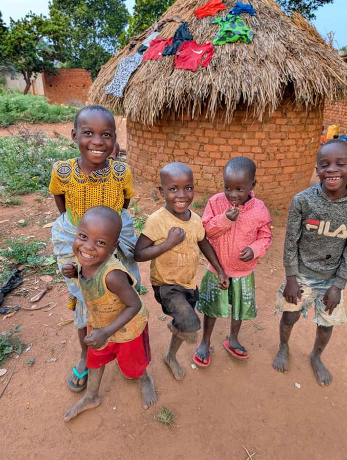 Children dancing and smiling outside a hut, showing joy and life in the midst of poverty.