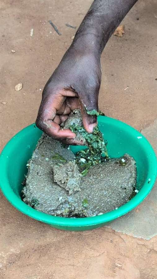 Children seated near plates containing dirt and greens, showing the severe poverty facing the community.