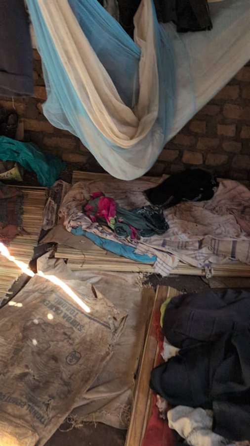 A simple interior with dirt floor, thin bedding, and makeshift sleeping arrangements instead of proper beds.